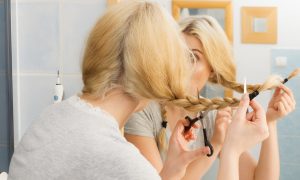 Žena strihajúca si nožničkami blond vlasy pred zrkadlom