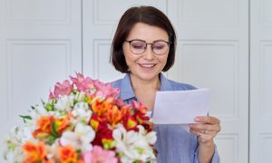 žena s kvetmi si číta blahoželanie