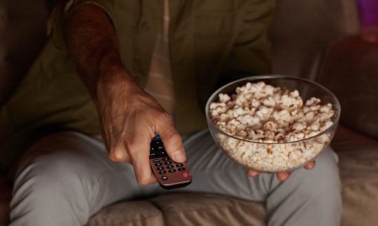 muž držiaci tv ovládač a misku s popcornom