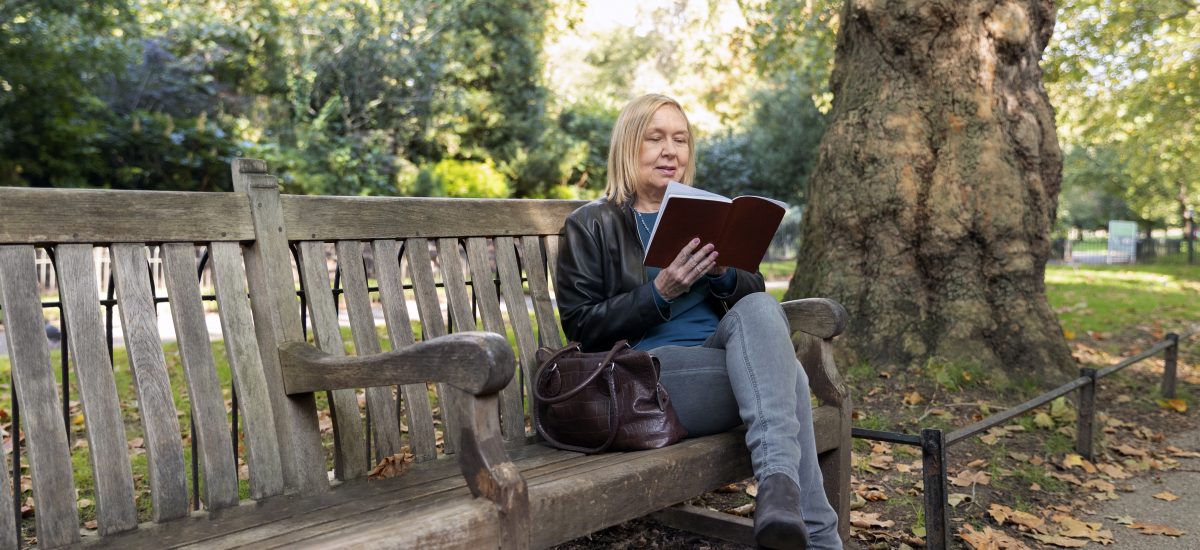žena sedí na lavičke v parku a číta si knihu
