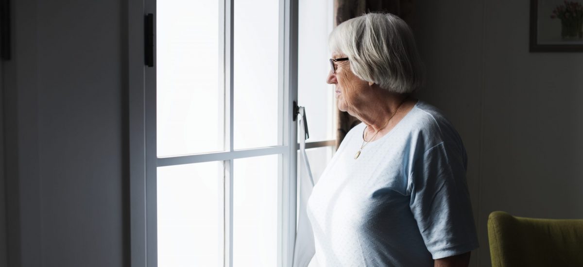 staršia pani stojí pri okne a pozerá sa von