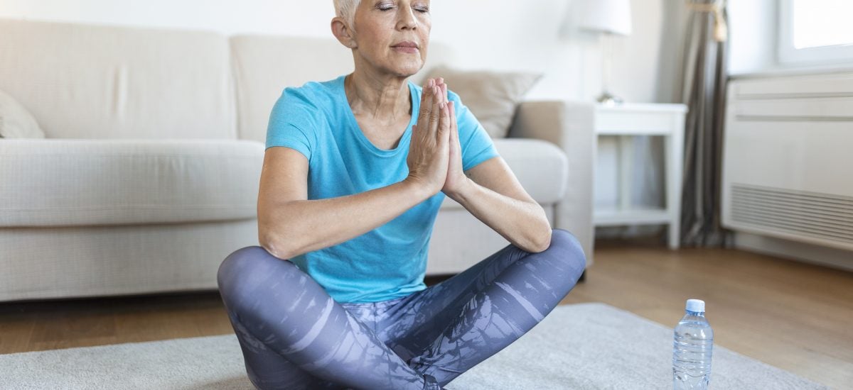 staršia pani sedí na koberci a cvičí jogu