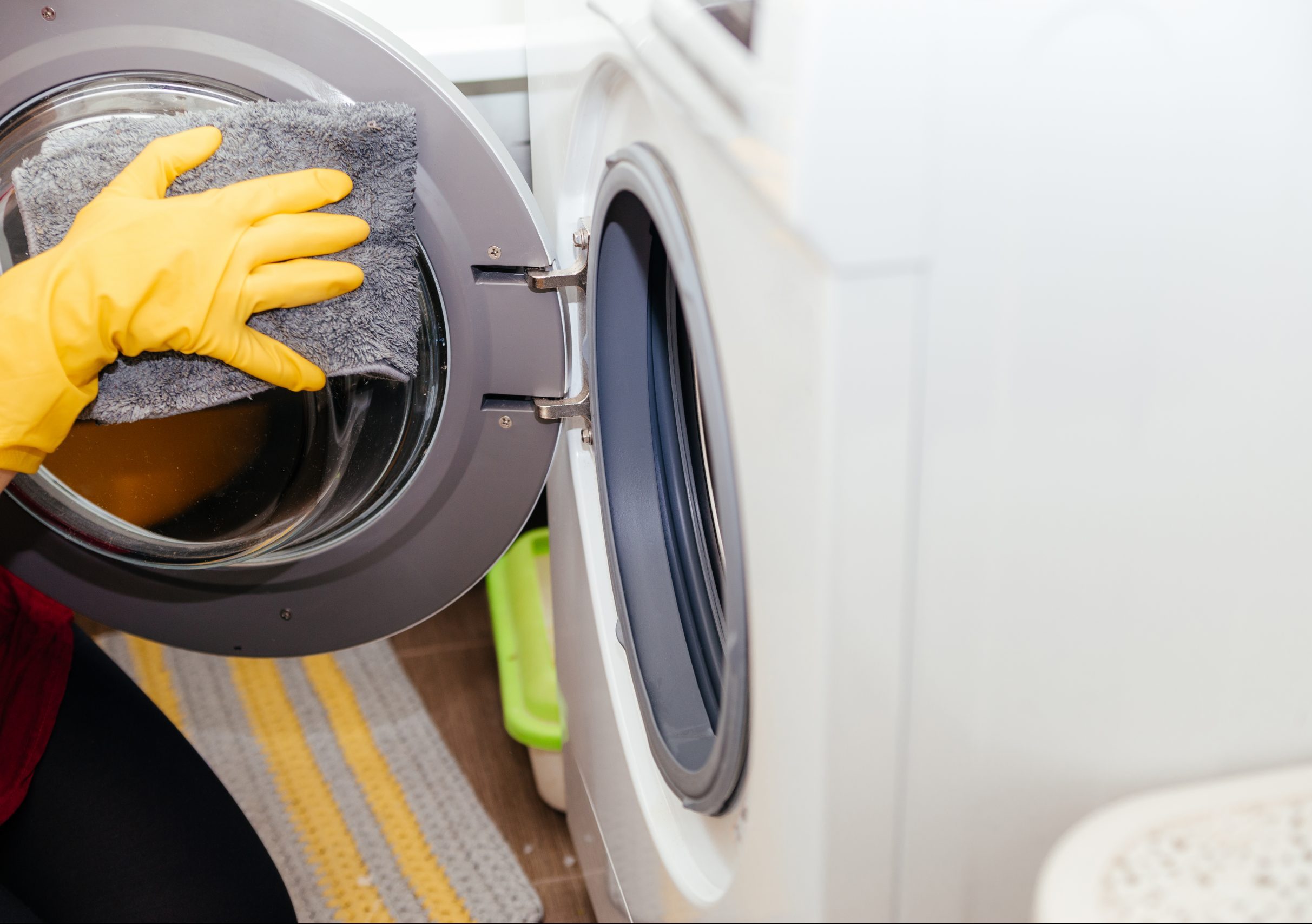 žena čistiaca práčku v žltých gumených rukaviciach