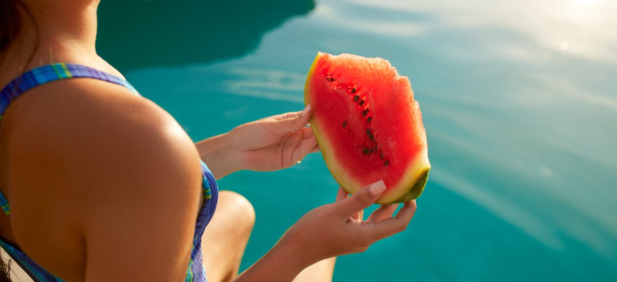 žena jediaca melón pri bazéne
