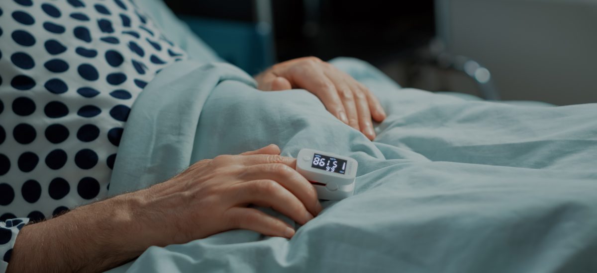 pacient leží na posteli, záber na oxymeter
