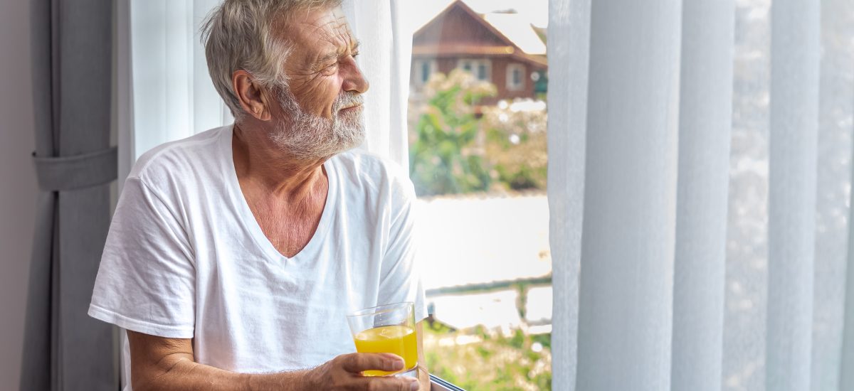 starší muž sa pozerá z okna s nápojom v ruke