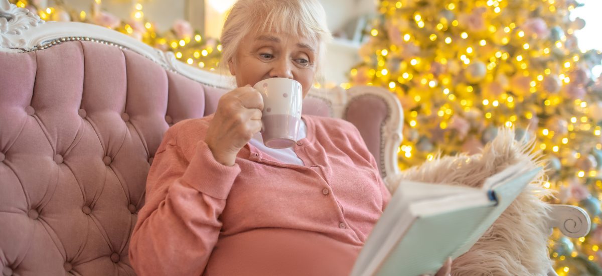 staršia žena číta knihu v izbe s vianočným stromčekom