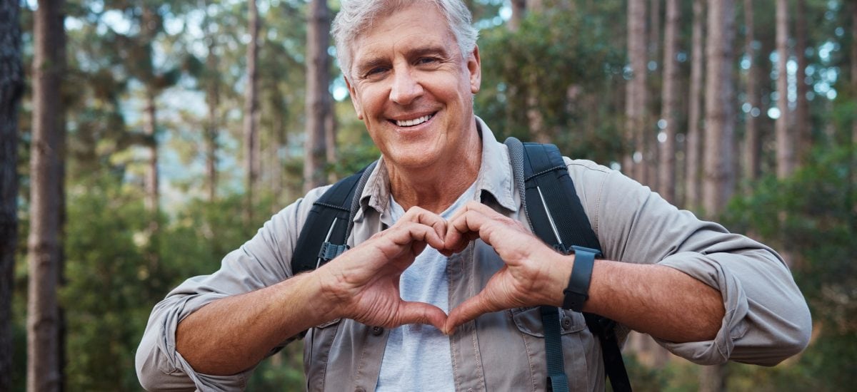 Muž v lese si drží ruky v tvare srdca.